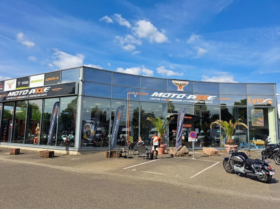 Photographie en intérieur d'atelier ou showroom d'Atout Motos montrant trois à quatre collaborateurs de l'entreprise en tenue professionnelle (polo ou chemise Atout Motos), souriant, interagissant ensemble autour d'une moto ou d'un client, incarnant l'esprit collectif, la camaraderie et la préparation à accompagner les motards au quotidien. Ambiance lumineuse et professionnelle, environment soigné caractéristique d'un atelier moderne.